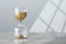 Hourglass with flowing gold sand on table against white wall, space for text