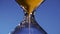 Hourglass golden sand in a transparent flask is poured on a blue background, punctuating the transience of time
