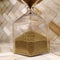 Hourglass made of clear glass, with gold beads. Sand pours down from top to bottom. Object on a wooden background of natural color