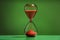 Hourglass with red flowing sand on green background