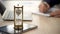 Hourglass standing on table with sand trickling, man working with graphs, data