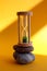 An hourglass stands on stones on a yellow background in the sun, side view, vertical frame