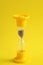 Hourglass in them sand running through glass containers on a yellow background with a copy of space