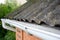 House asbestos roof with close up gutter holder and plastic roof gutter pipe. Guttering