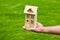 House in caring female hands. Man holding wooden model house in hands on grass background.