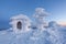 The house is covered with snow and ice of a textural mysterious form on a snowy lawn against a background of blue sky. Winter.