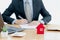 A House on desk envelope with man signing purchase documents in background. while hand complete the insurance policy, rental