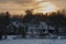 House at the foot of the hill, among the trees, during snowfall, at sunset.