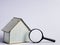 House miniature with magnifying glass against white background. Property inspection or investment.