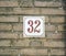 House Number 32 thirty two. brown numbers on a white plate constructed to a old brick wall