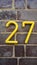 House number on the brick wall - twenty seven in yellow numerals