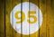 House number or calendar date in white circle on yellow toned wooden door background. Number ninety five 95