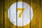 House number or calendar date in white circle on yellow toned wooden door background. Number seven 7