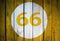 House number or calendar date in white circle on yellow toned wooden door background. Number sixty six, 66