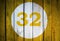 House number or calendar date in white circle on yellow toned wooden door background. Number thirty two 32