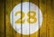 House number or calendar date in white circle on yellow toned wooden door background. Number twenty eight 28