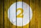 House number or calendar date in white circle on yellow toned wooden door background. Number two 2