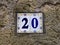 House number twenty 20: ceramic tiles with blue figures on old stone wall.