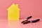 House renovation concept. Home repair and redecorated. Lineman pliers, screws and yellow house shaped figure on pink background