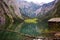 House on the shore of a large Obersee lake in the Alps with logs and stones