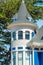 House spire with blue and white accent paint with round roof with gray tiles and foliage and blue sky background in