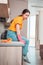 A housewife in casual clothing and rubber gloves sits on the kitchen table, resting after cleaning. Side view