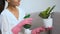 Housewife in gloves watering potted flower leaves with spray, caring plants