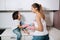 Housewife mom in pink gloves washes dishes with her son by hand in the sink with detergent. A girl in white and a child