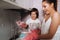 Housewife mom in pink gloves washes dishes with her son by hand in the sink with detergent. A girl in white and a child