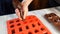 A housewife pours liquid chocolate into a candy mold. The man lays out in the form of cherries in cognac. Homemade chocolates with