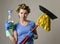 Housewife stereotype hair rollers and washing gloves holding mop broom and detergent spray bottle