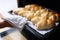 Housewife taking hot delicious mouth watering buns out of oven on baking sheet closeup