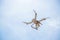 Hovering drone against clear blue sky with clouds taking pictures.