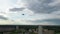 A hovering drone takes off against a cloudy sky and forest background.The quadcopter is flying towards the forest and