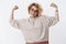 How strong girl is. Portrait of enthusiastic happy and confident european blond woman in glasses and sweater showing