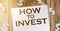 How to invest words written on copybook page and paper dollar signs around. Saving and investment business concept