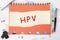 HPV word is written on a sheet in a cage lying on a notebook on the table next to stationery