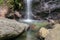 Huge boulders and pieces of rock falling into a pond under a waterfall. Pure water from a mountain river flows down a rock. Moss