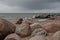 Huge boulders on the shore of the bay, on the coast of the sea. A wave, a cloudy pre-storm sky, an expressive relief living landsc