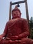 Huge cement plaster red statue of sitting Buddha, which stands 18 feet tall.