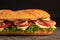 Huge fresh crispy baguette sandwich with meat, prosciutto, cheese, lettuce salad and vegetables. Close up. Black background. Space