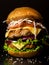 Huge homemade burger with two cutlets and fresh vegetables on a dark background