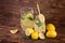 A huge jug and glass full of fresh summer lemonade with yellow, ripe, and juicy lemon and fresh green mint on a dark wooden table.