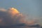A huge large cumulus high stormy gray cloud, the top of which turns orange during the early morning summer sunrise.