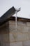 Huge long icicle hang on a drainpipe in overcast sky background