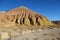 A huge sandy-clay multi-colored mountain with relief slopes in the Altyn-Emel National Park on a sandy plateau against the sky,