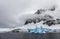 Huge steep stone rock covered with glacier and drifting blue ice