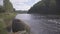 Huge stone perched near riverbank, dark forest is across the river.