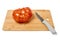 Huge tomato with a kitchen knife on a chopping board isolated on white background