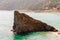 Huge triangle shape rock in the water on the beach with famous cityscape of Monterosso Al Mare and high green mountains on the